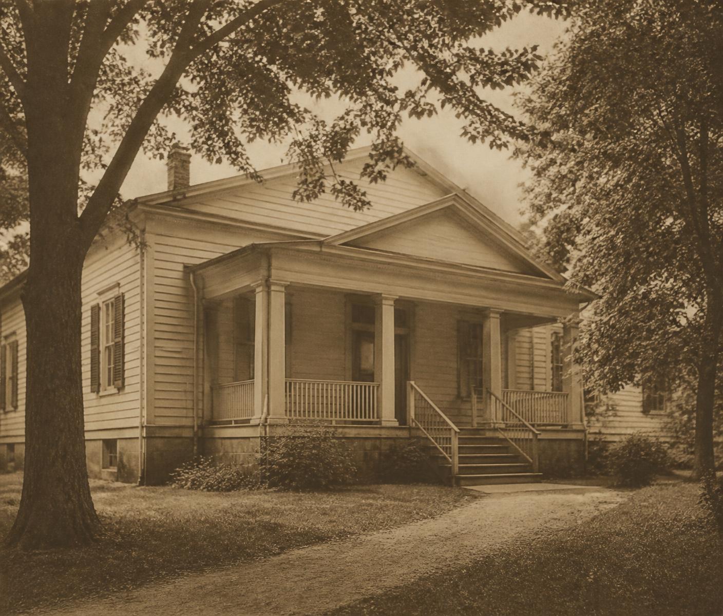 Sepia-toned archival photograph of a modest historic community house with a covered porch